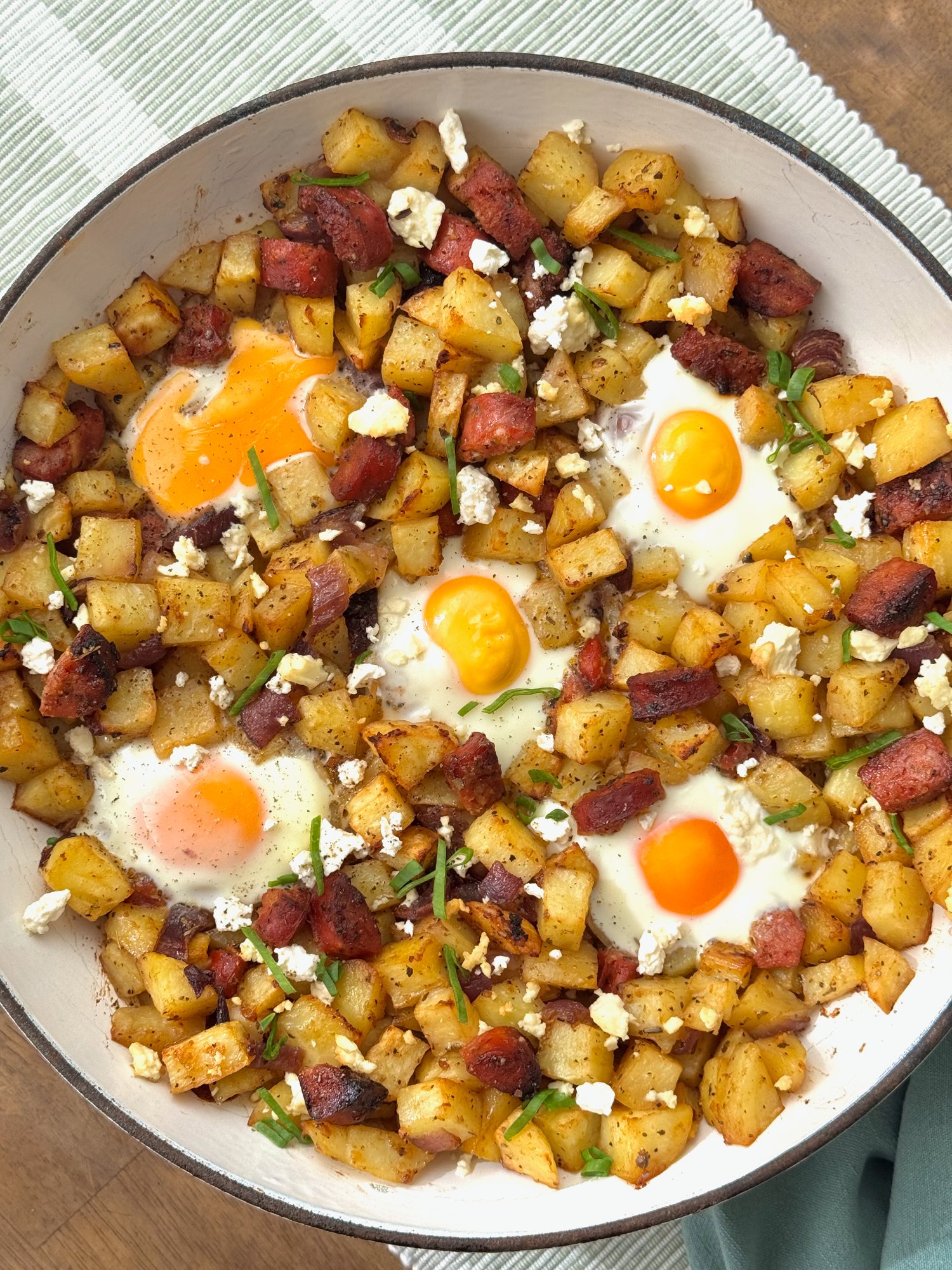 A breakfast skillet of roasted potatoes, chorizo and baked eggs with feta and spring onion.