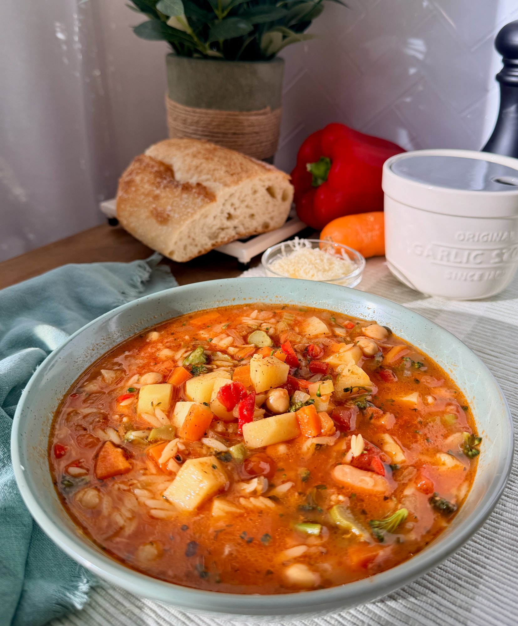 A bowl of minestrone with vegetables, beans, risoni, parmesan and olive oil.