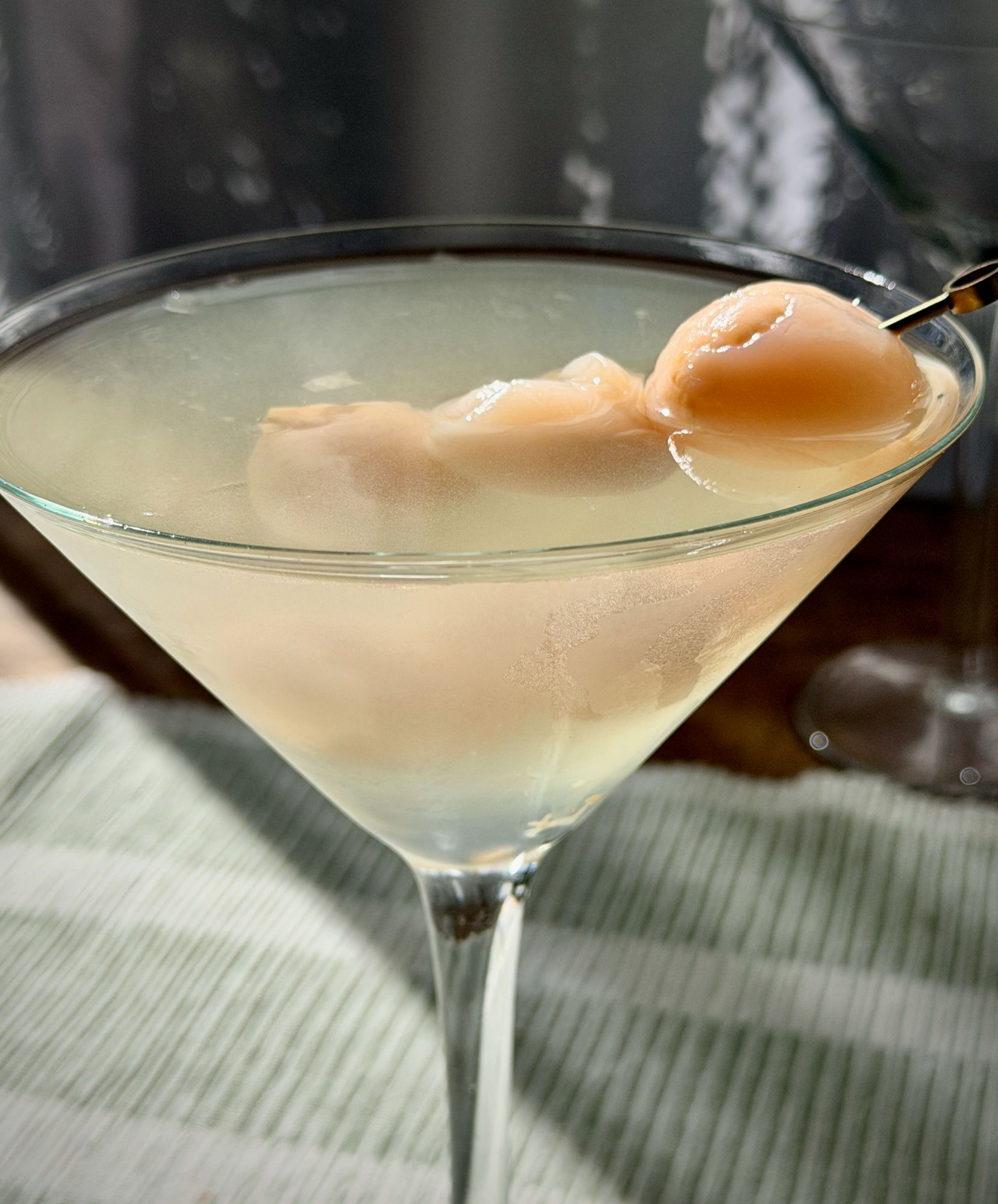 A lychee and elderflower martini in a chilled glass, garnished with whole lychees on a pick.
