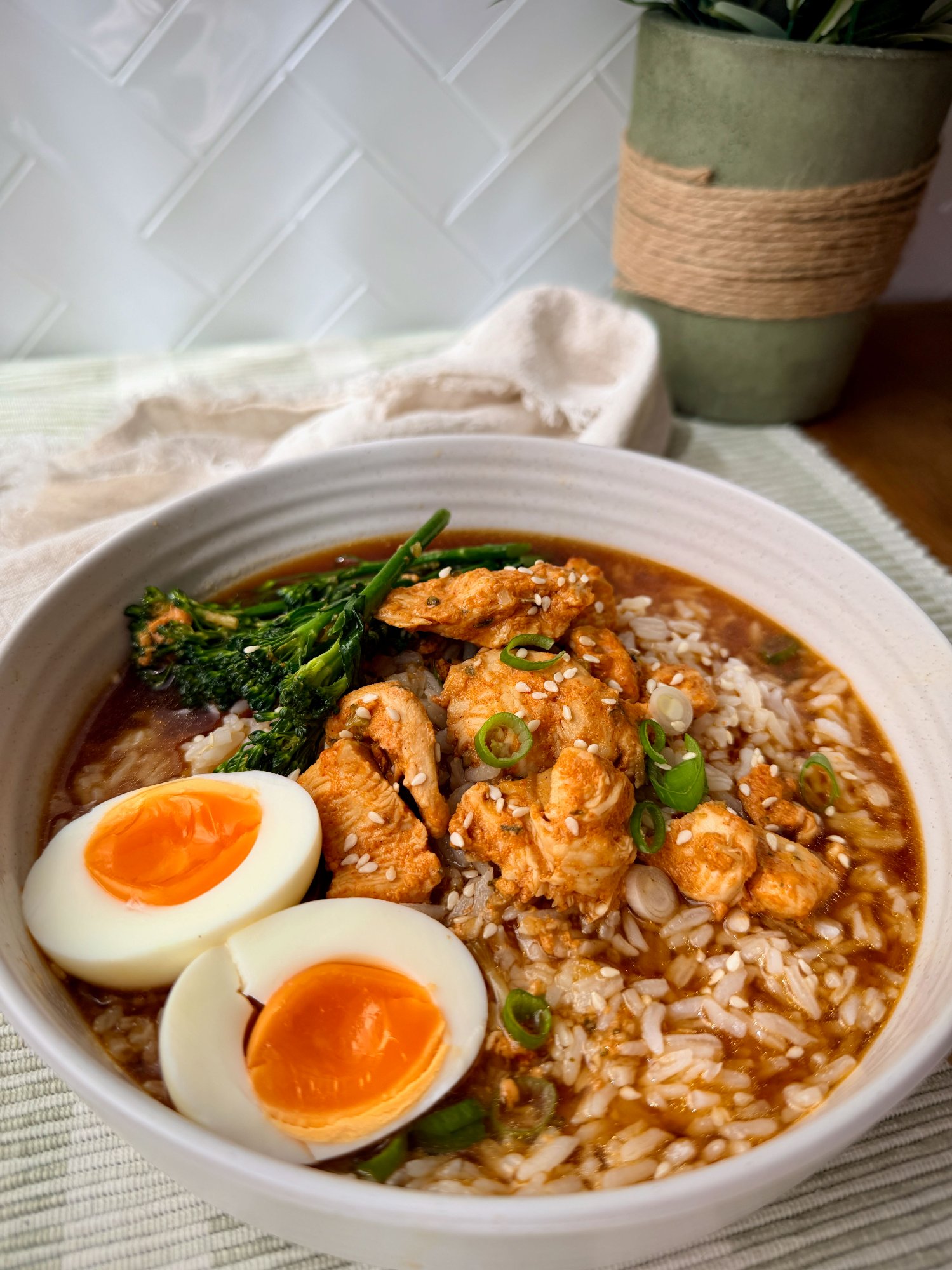 A bowl of chicken, rice and broccolini in ginger bone broth with a halved soft boiled egg.
