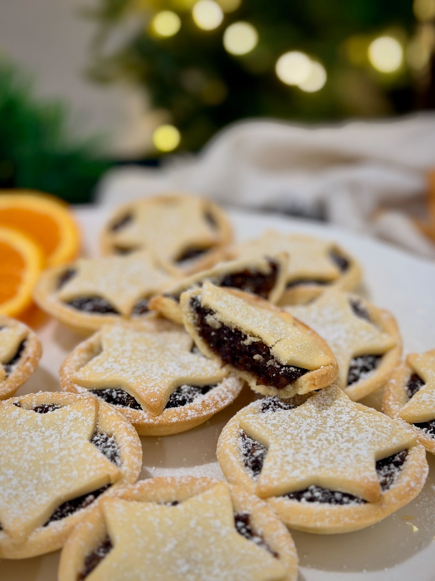 Christmas mince pies with pastry star tops and icing sugar, one cut open to show the dark fruit filling.