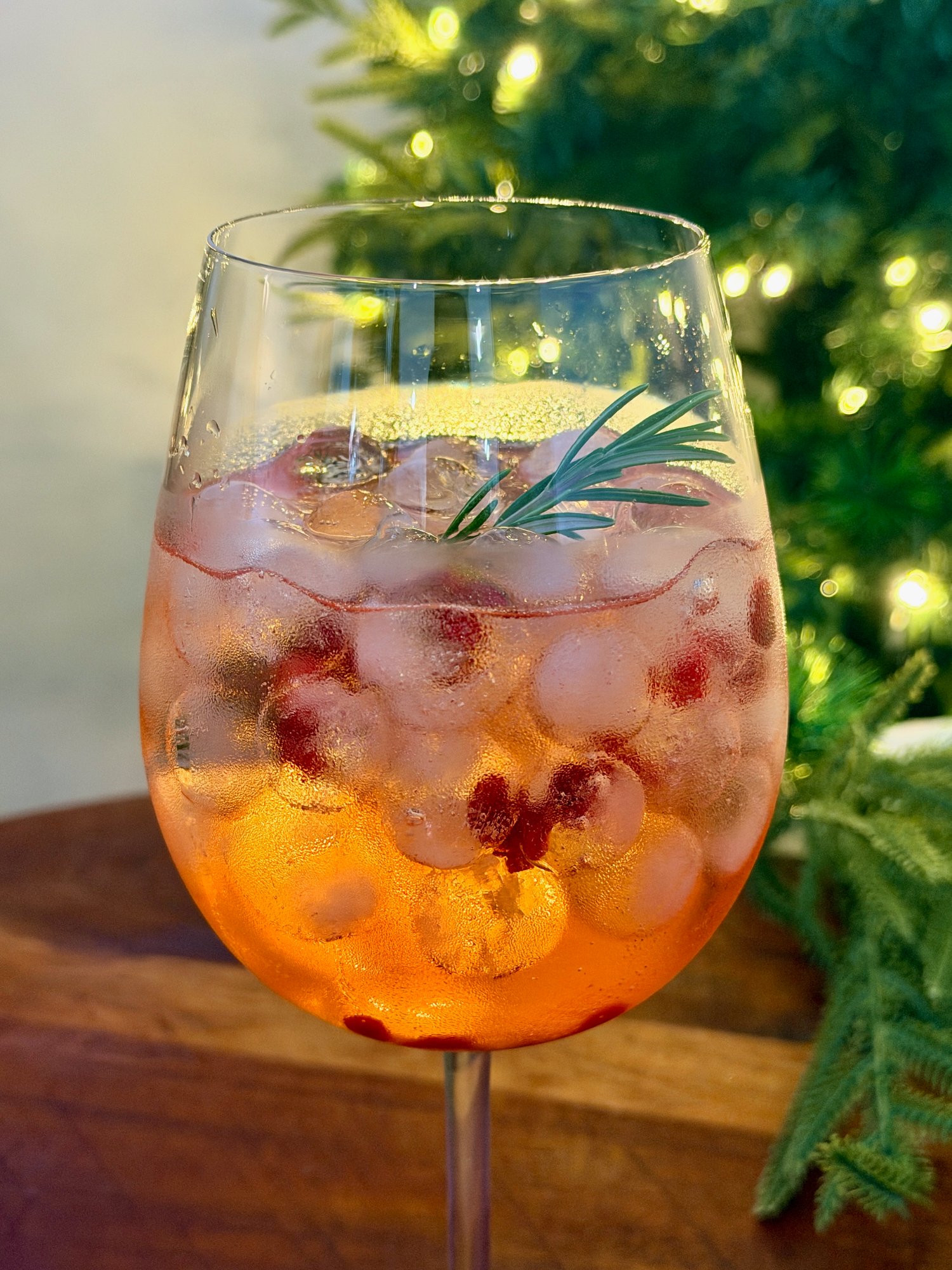 Christmas Negroni Spritz in a large wine glass over ice, with pomegranate arils and a sprig of fresh rosemary