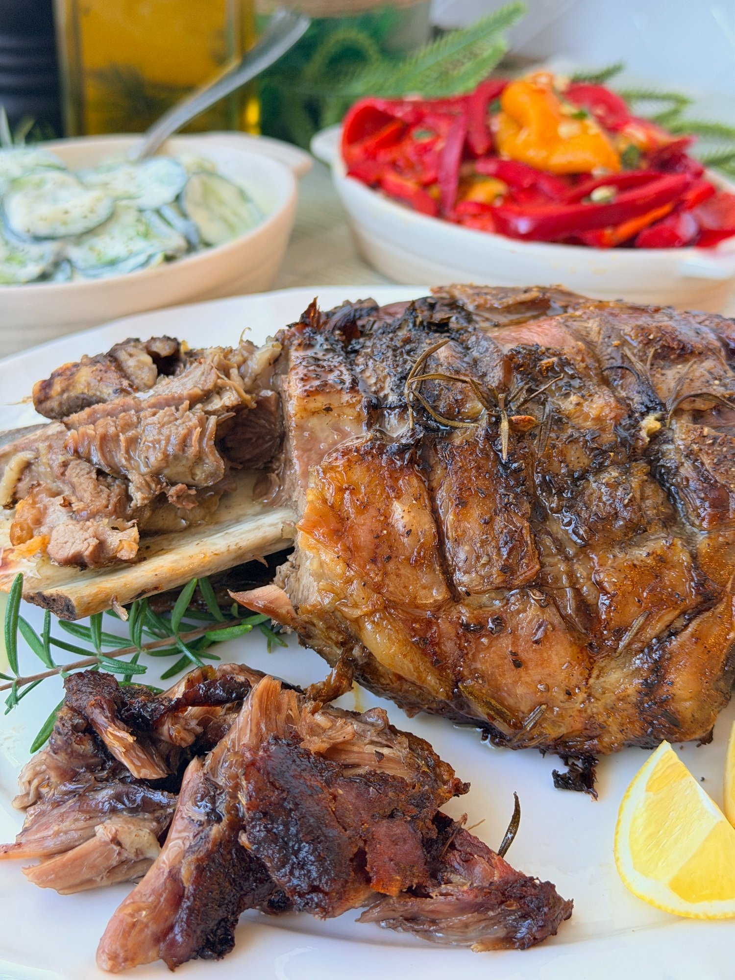 Slow-roasted garlic and rosemary lamb shoulder with pulled meat, lemon wedges and rosemary, served with roasted capsicum salad and cucumber yoghurt salad.