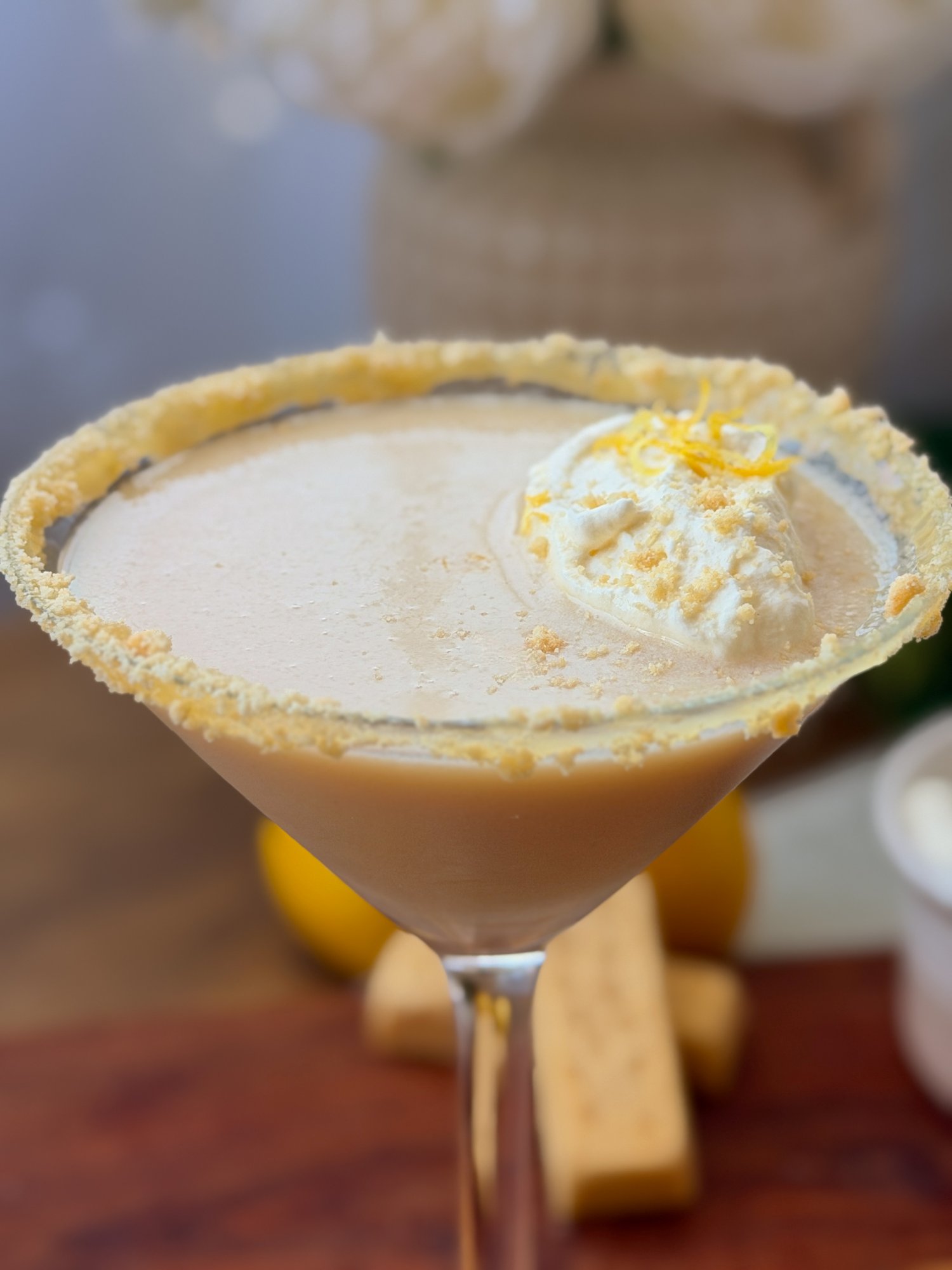 Christmas lemon meringue and shortbread martini in a shortbread-rimmed glass, topped with whipped cream, crushed shortbread and lemon zest