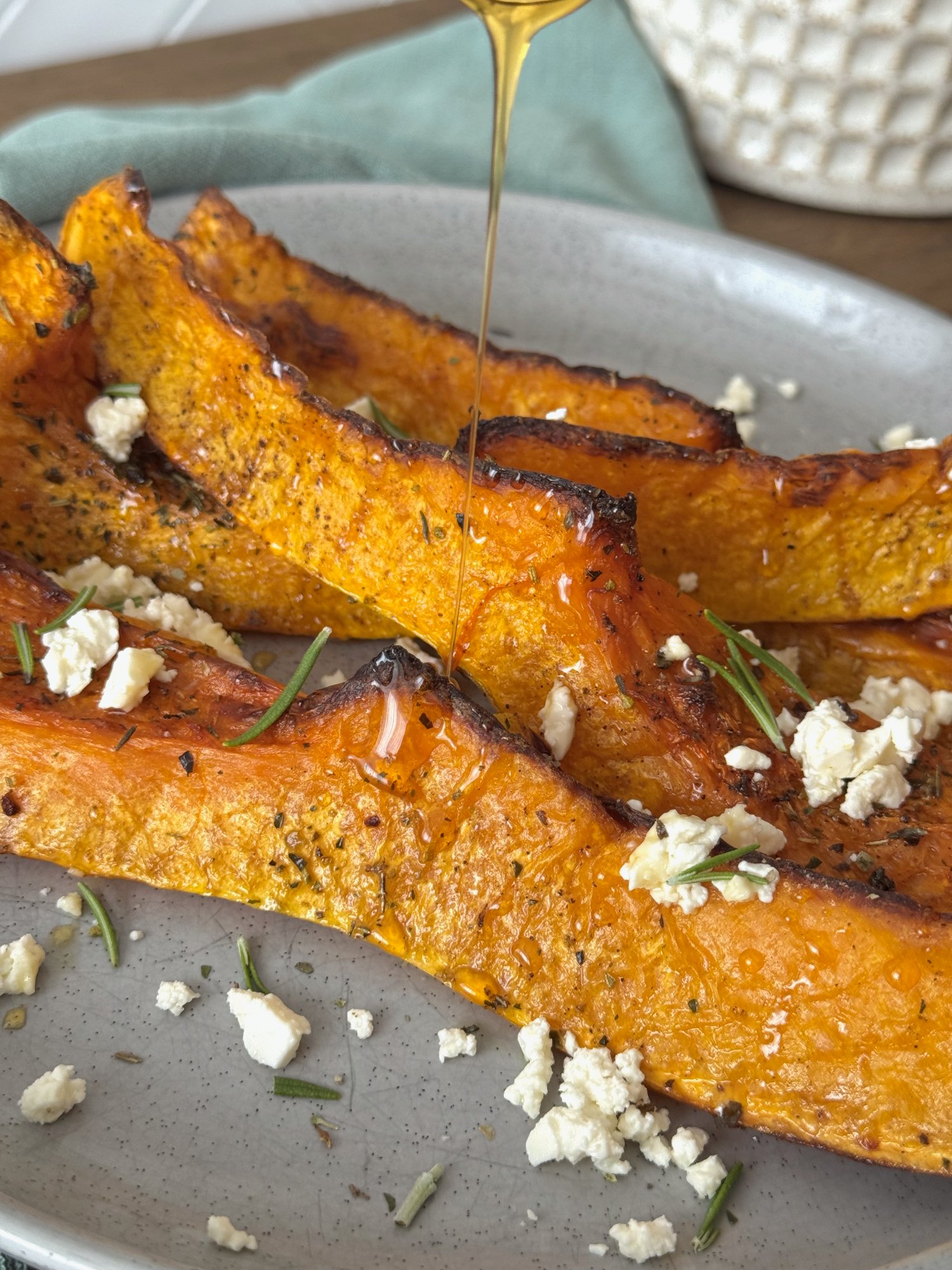 Roasted pumpkin wedges with golden edges, topped with crumbled feta, fresh herbs and honey.