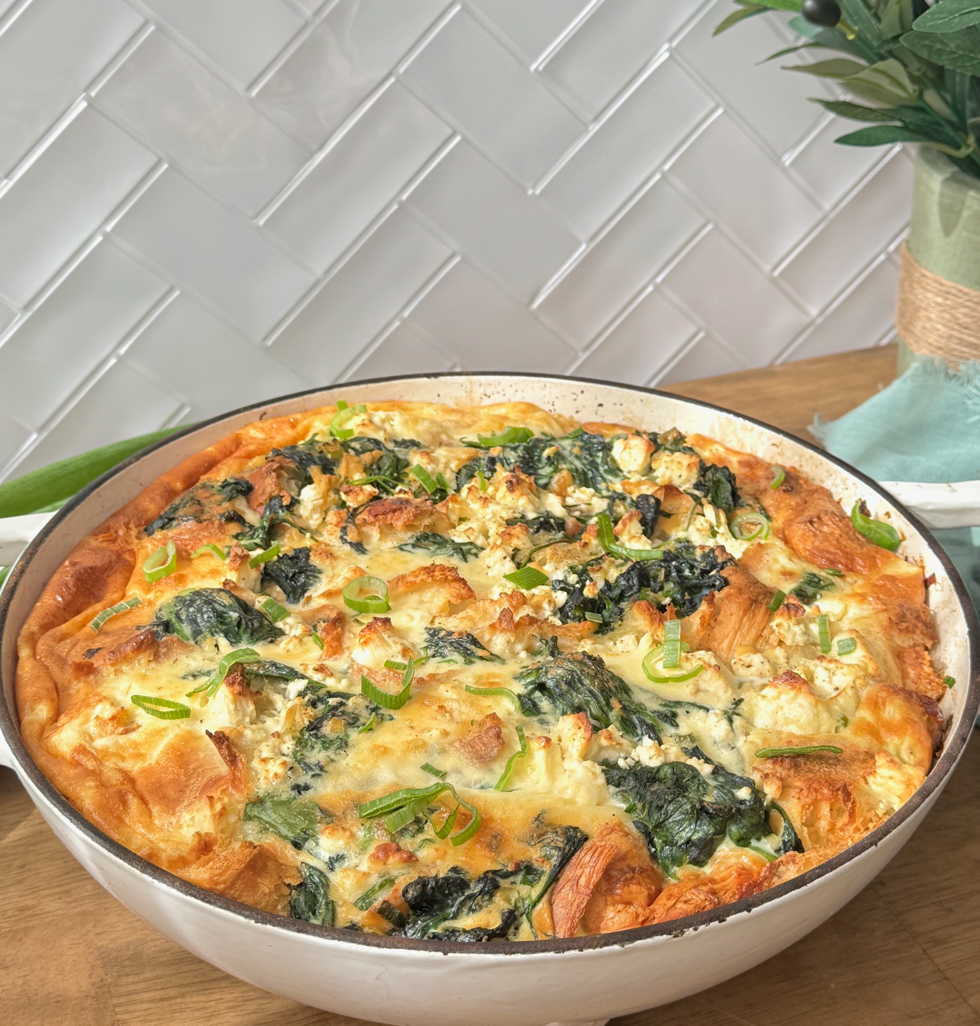 A golden spinach, feta and spring onion croissant bake in a baking dish.