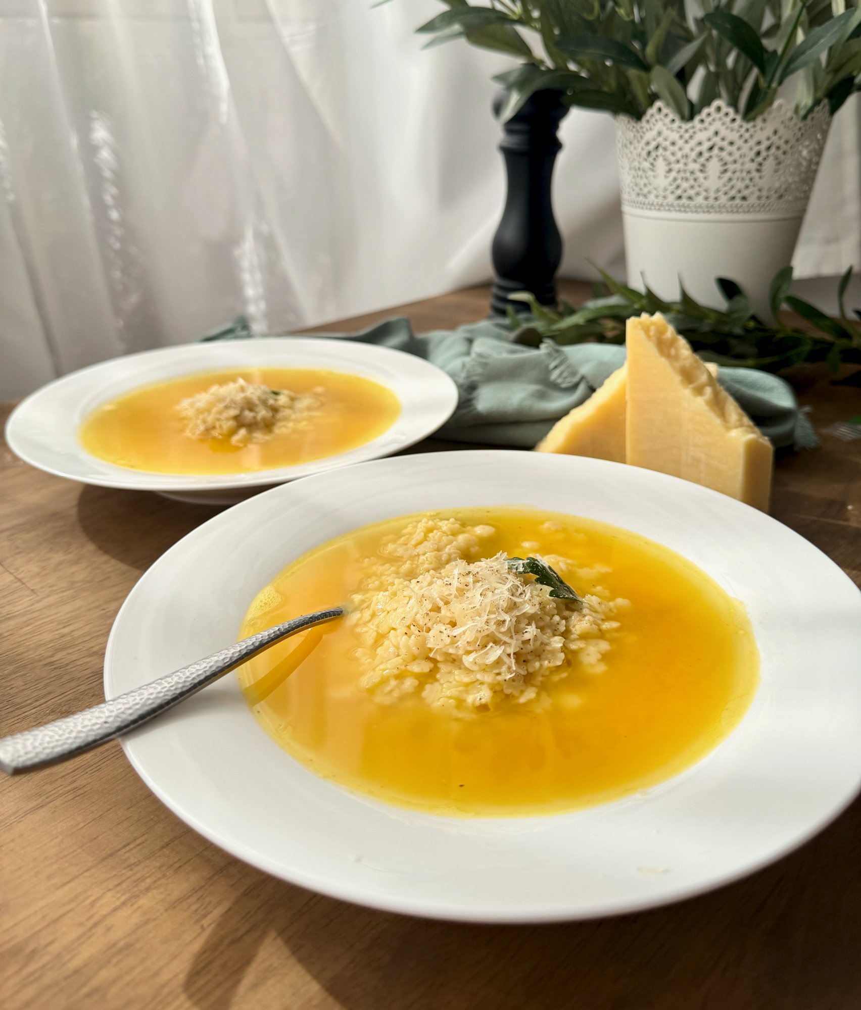 A bowl of golden pastina soup with tiny star pasta, grated parmesan and cracked black pepper.