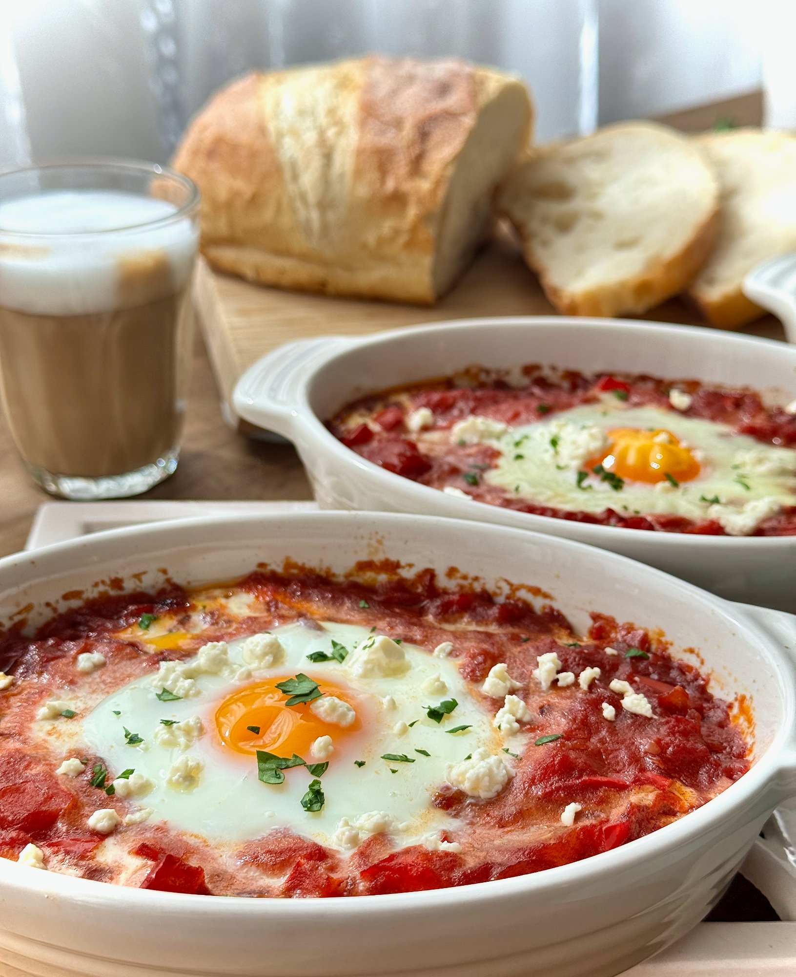 Mini Portuguese baked eggs over a red tomato and capsicum base, topped with crumbled feta and parsley.