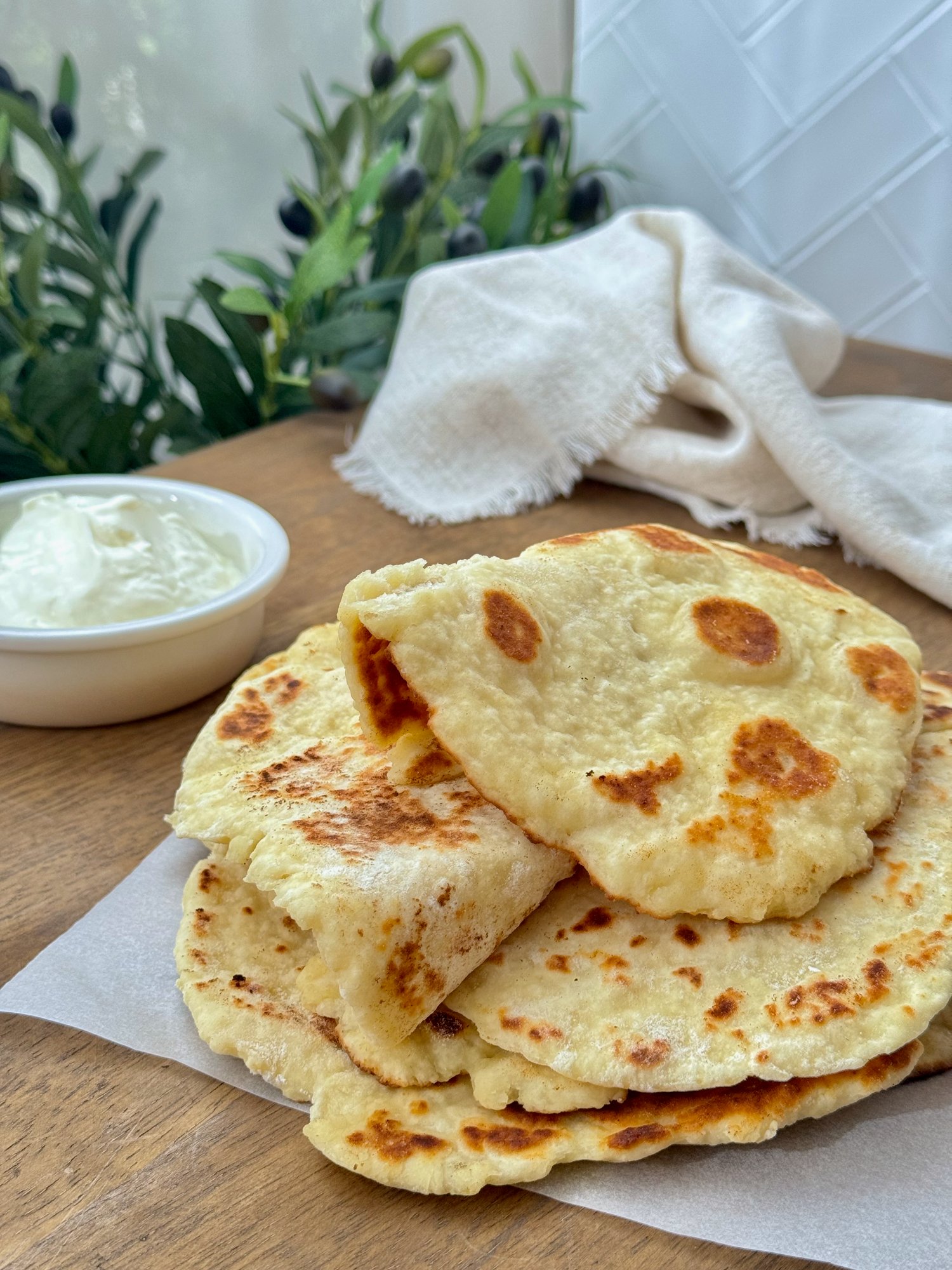 A stack of soft, golden Greek yoghurt flatbreads with charred spots.